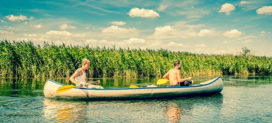 To mænd sejler kano på en å i solskin