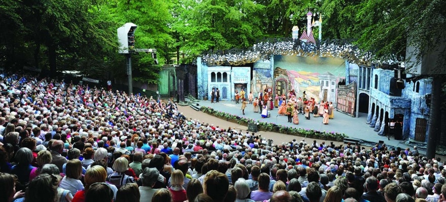 Hundredevis af tilskuere kigger på teater. Et udendørs tearterstykke midt i skoven.