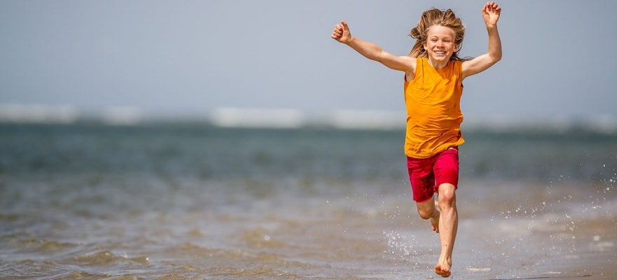Glad dreng løber med armene over hovedet langs vandkanten på stranden