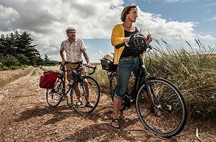 Kvinde og mand står på en sti med deres cykler i solskin